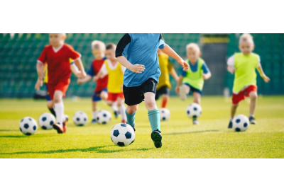 children kicking footballs and running on a field